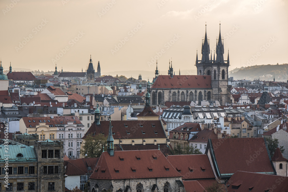 Amazing landscape of Prague, with a view of the roofs, the spires and the towers of the medieval town, everything set under a magical warm orange and yellow dusk sky