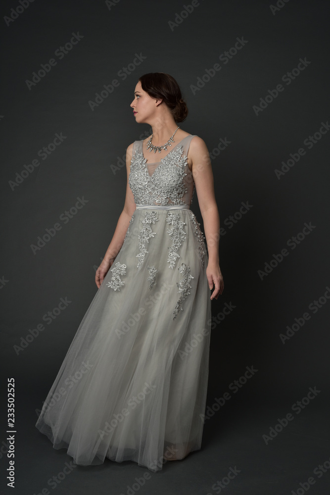 full length portrait of brunette girl wearing long silver ball gown. standing pose on grey studio background. full length portrait of brunette girl wearing long silver ball gown. standing pose on grey studio background.