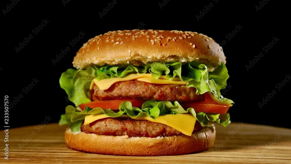 Fresh appetizing hamburger rotating on black background. Seamless loopable shot, 4k.