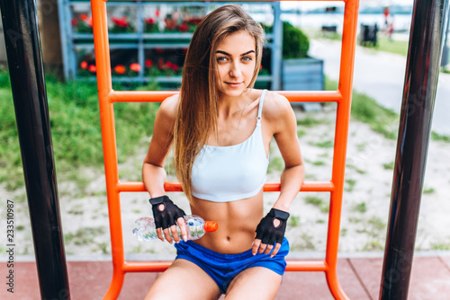 Cute sporty girl relaxing after outdoor training with bottle of water in hands