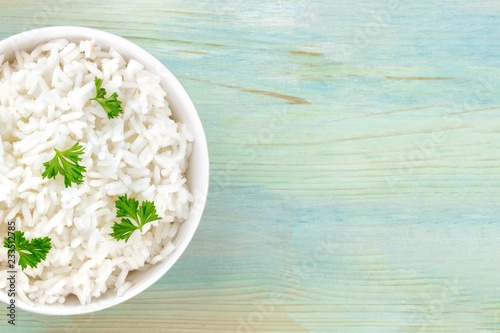 A closeup photo of a bowl of cooked white long rice, shot from above on a teal blue background with a place for text