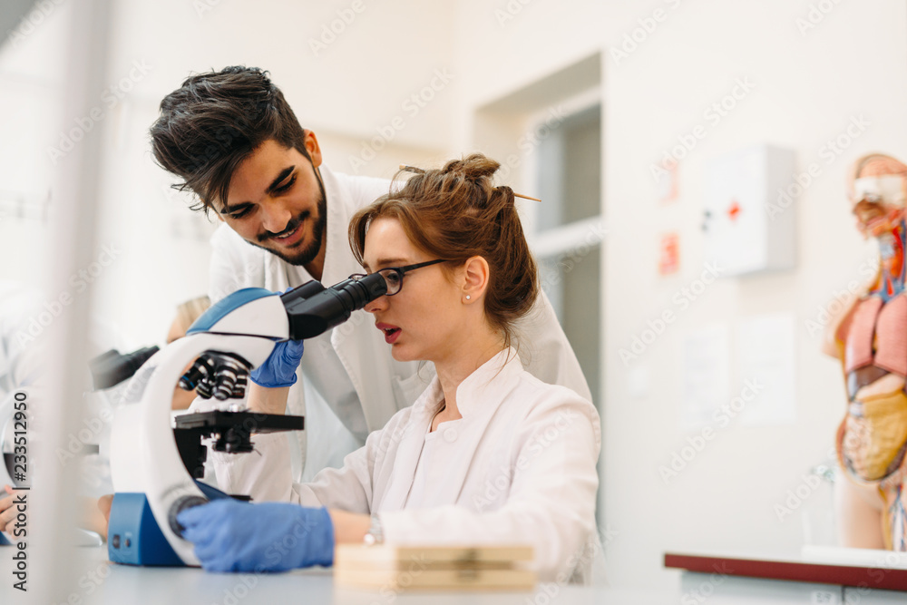 Fototapeta premium Young scientist looking through microscope in laboratory
