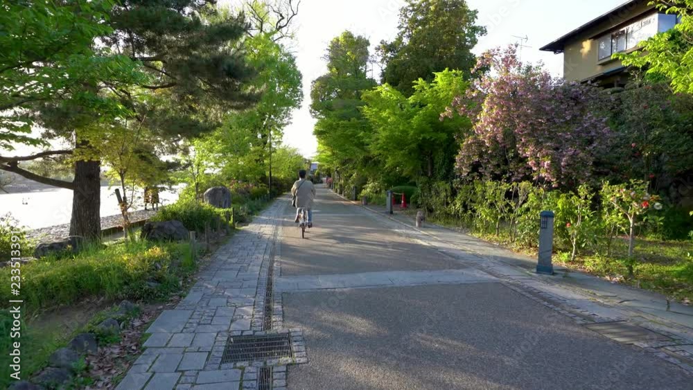 Japanese man riding bike in the path and two high school students wearing uniform standing beside the river Japanese man riding bike in the path and two high school students wearing uniform standing beside the river