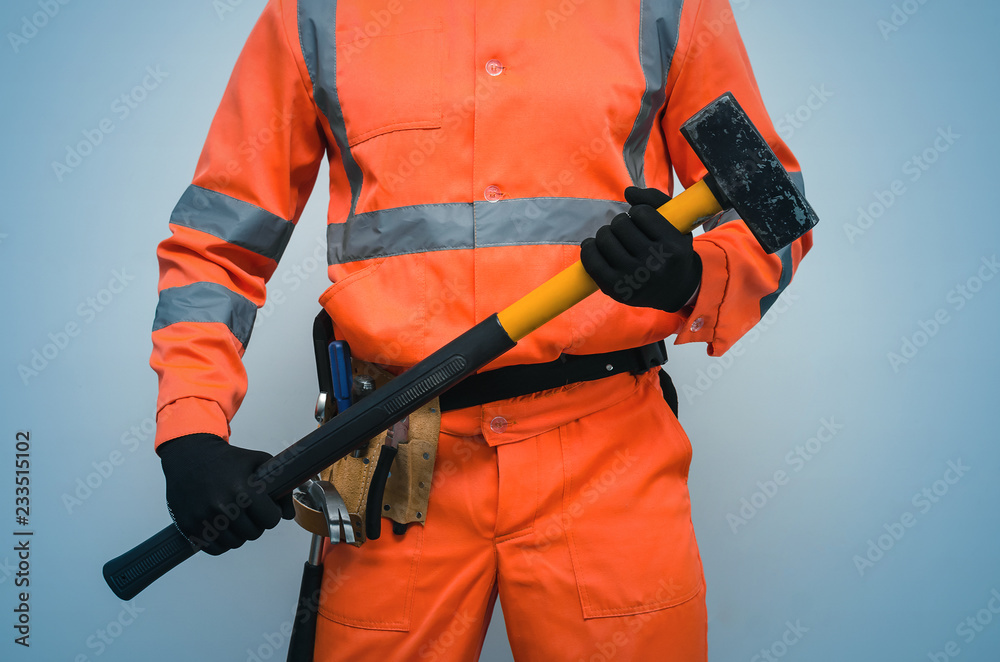 Builder worker holding in hands a big sledgehammer isolated on blue background. Under construction concept. Builder worker holding in hands a big sledgehammer isolated on blue background. Under construction concept.