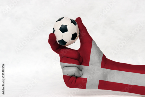Mini ball of football in Denmark flag painted hand, hold it with two finger on white background. Concept of sport or the game in handle or minor matter. photo