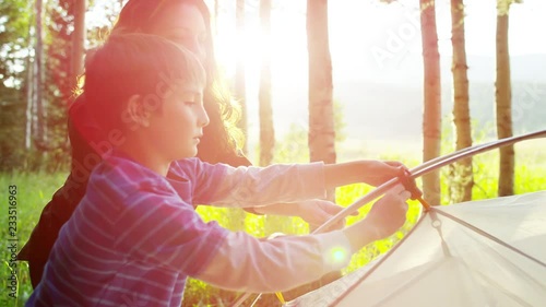 Happy American Caucasian mother and son erecting tent in woodland on vacation