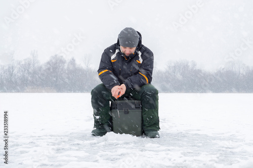 Winter fishing concept. Fisherman in action, catching fish from ice in snowy weather.