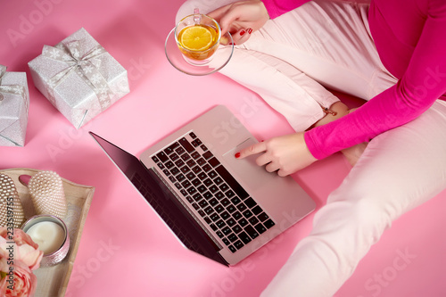 top view of female hands on a laptop keyboard, candles, flowers and gifts on a light pink background
