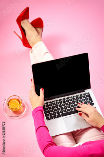 female hands on a laptop keyboard, businesswoman in red high heels, on a light pink background