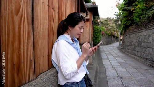 beautiful female tourist relying on the wooden wall and using cellphone photo