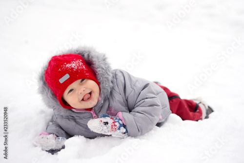 Child lies in the snow and shows tongue.