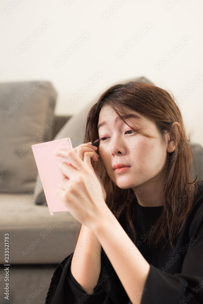 Asian young woman looks into pink pocket mirror and putting eye pencil color on eyes. Makeup beauty care woman. Asian young woman looks into pink pocket mirror and putting eye pencil color on eyes. Makeup beauty care woman.