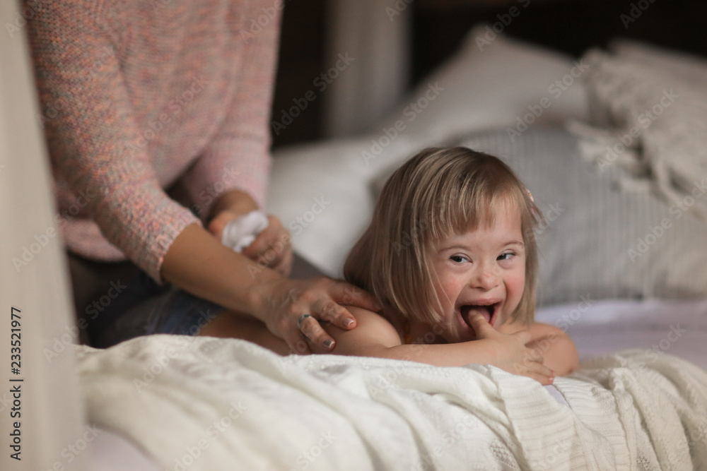 mom massage to child with Down syndrome on bed