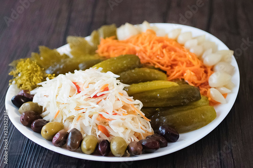 Assorted pickled and fermented vegetables in a white plate on a brown wooden background.