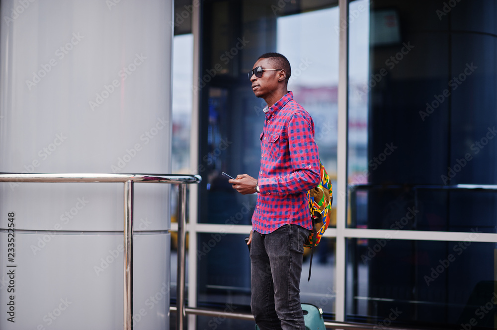 African american man in checkered shirt, with suitcase and backpack. Black man traveler against bus station.