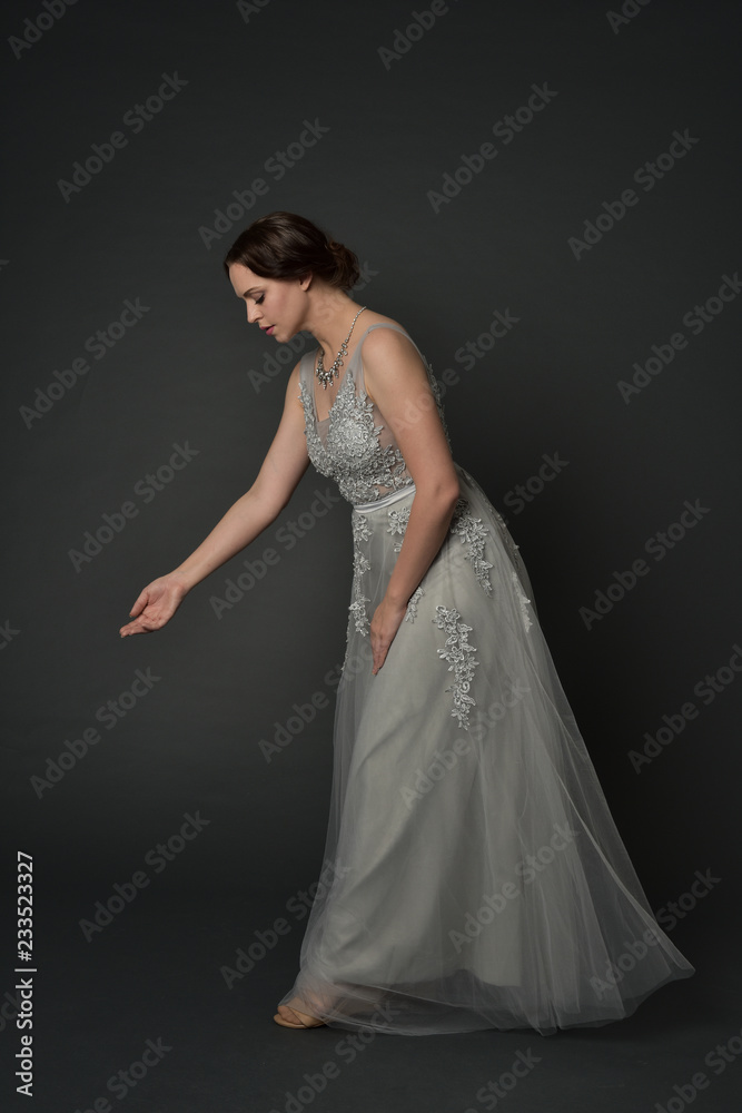 full length portrait of brunette girl wearing long silver ball gown. standing pose on grey studio background. full length portrait of brunette girl wearing long silver ball gown. standing pose on grey studio background.