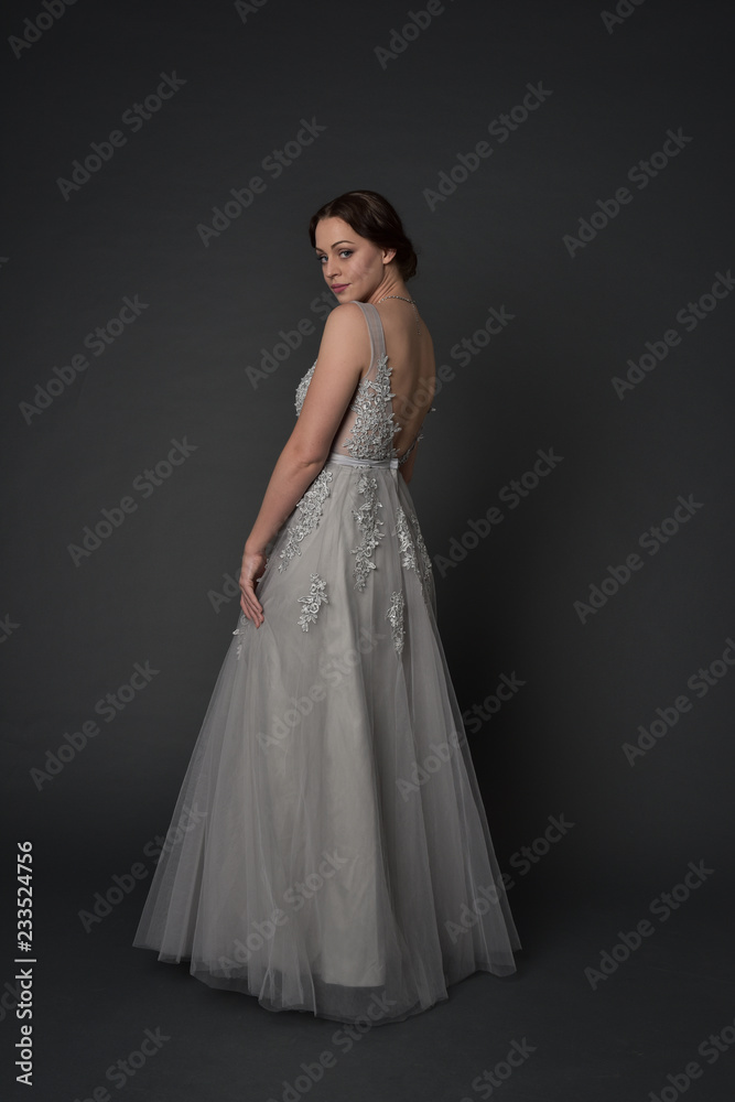 full length portrait of brunette girl wearing long silver ball gown. standing pose on grey studio background. full length portrait of brunette girl wearing long silver ball gown. standing pose on grey studio background.