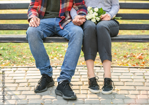 Loving young couple holding hands while sitting on wooden bench outdoors © Pixel-Shot