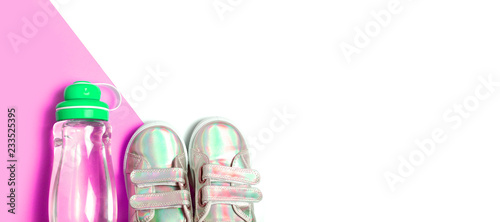 Child sneackers and bottle of water on pink and white background. photo