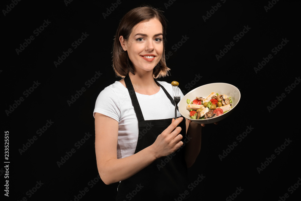 Young female chef with salad on dark background