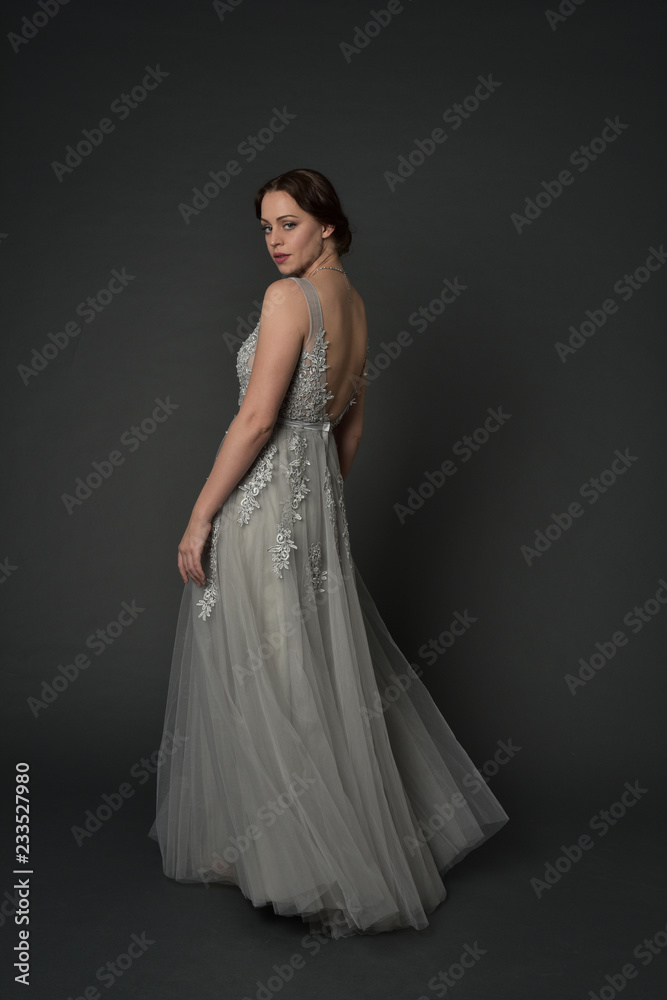 full length portrait of brunette girl wearing long silver ball gown. standing pose on grey studio background. full length portrait of brunette girl wearing long silver ball gown. standing pose on grey studio background.