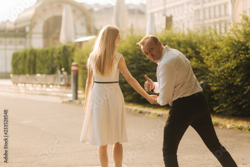 Young beautiful couple husband in a white shirt and a woman in a dress walking around the park in summer time