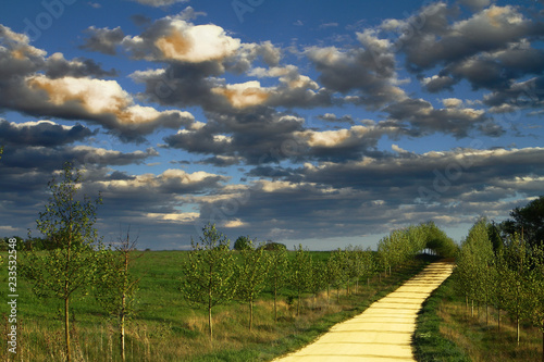 Beautiful yellow sand lane in countryside, green meadow on evening blue sky with clouds