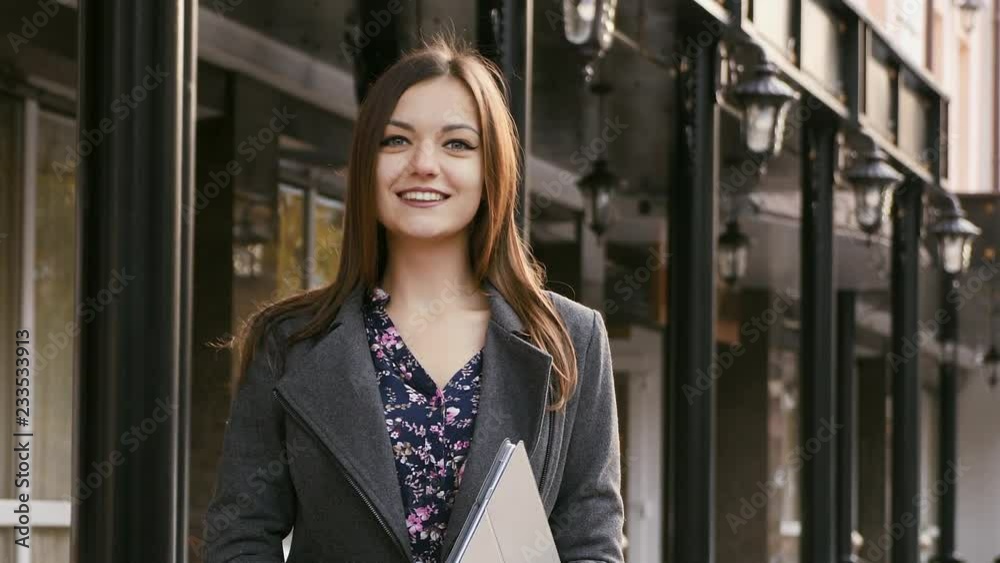 Portrait of young beautiful young businesswoman looking at camera with smile outdoors, standing near the hotel, in the hands holding a tablet, slow motion Portrait of young beautiful young businesswoman looking at camera with smile outdoors, standing near the hotel, in the hands holding a tablet, slow motion