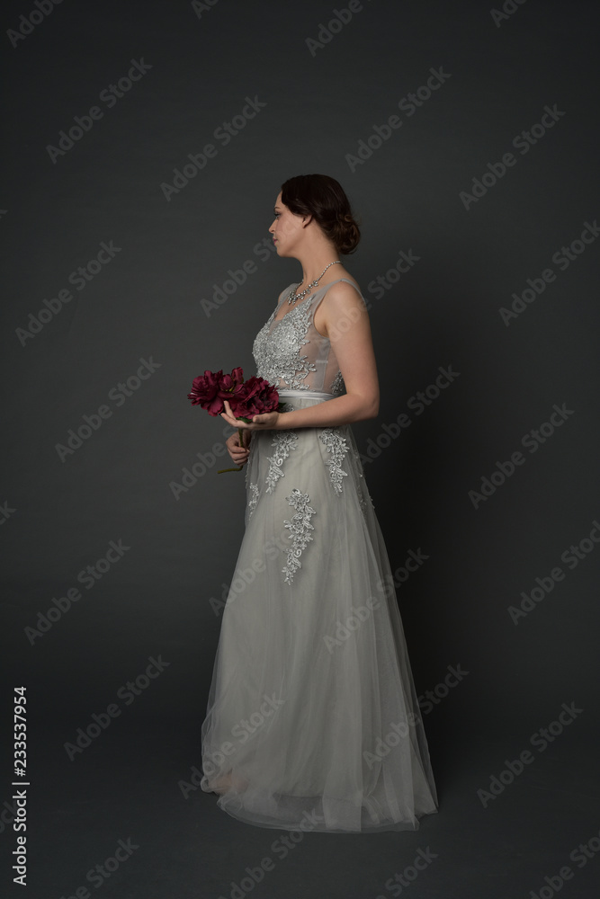 full length portrait of brunette girl wearing long silver ball gown. standing pose on grey studio background. full length portrait of brunette girl wearing long silver ball gown. standing pose on grey studio background.