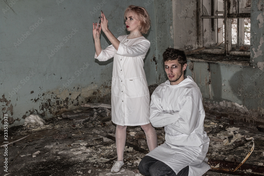 Asylum nurse or doctor with a syringe in hand is preparing to give an injection to an insane psycho patient in a straitjacket, inside of abandoned ruined hospital. Some horror movie scene