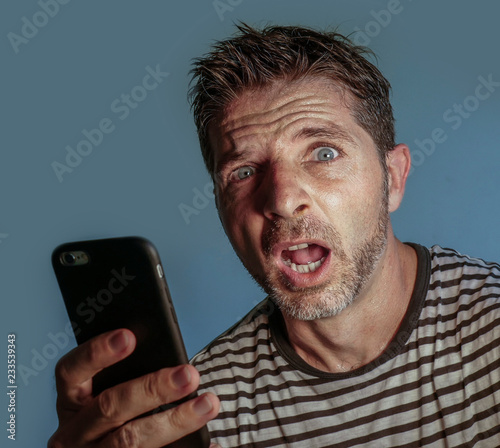 young weird and crazy mobile phone addict man using cell compulsively with weird and freak face expression in internet social media addiction and obsession