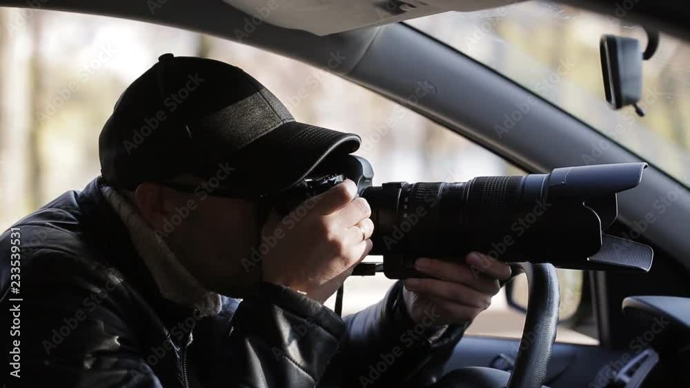 Private detective man sitting inside car and photographing with dslr camera