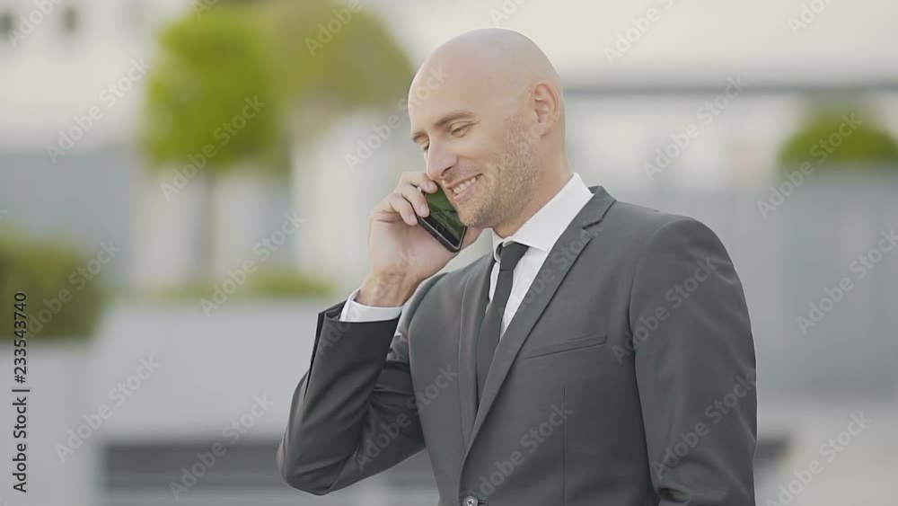 Smiling businessman answering and talking by smartphone. Handsome Caucasian manager talking on street. Communication concept Smiling businessman answering and talking by smartphone. Handsome Caucasian manager talking on street. Communication concept