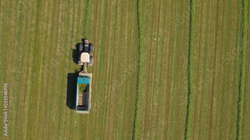 AERIAL: Farmer in tractor working on farm field and collecting fodder in swaths