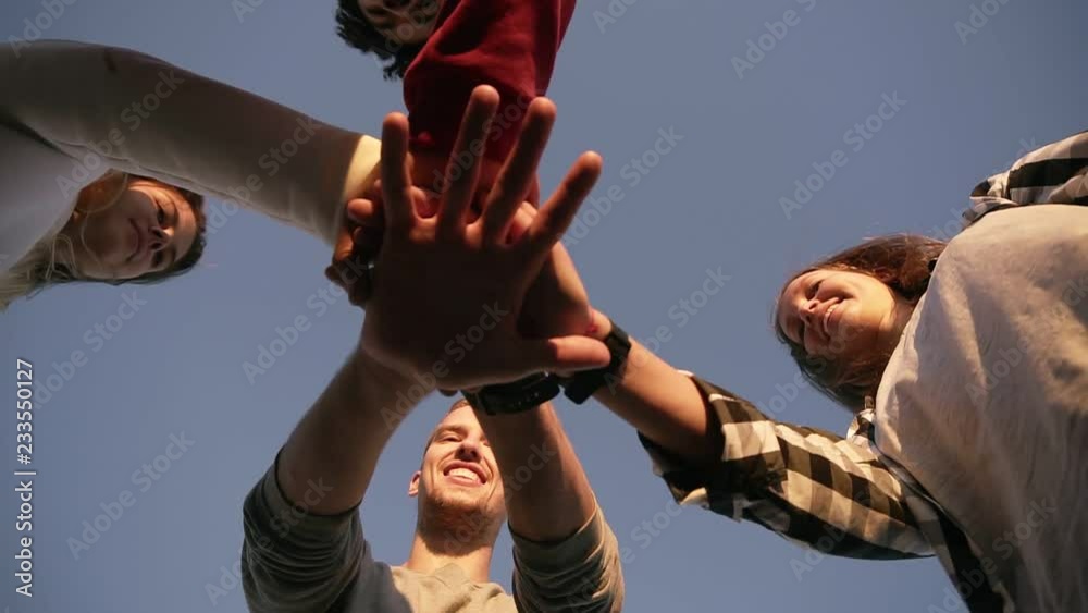 Four young friends looking down on ground posing on sunny day, putting hand on hand. Team work. Stylish youth, happy friendship hanging out together and smiling. Friendship, team concept