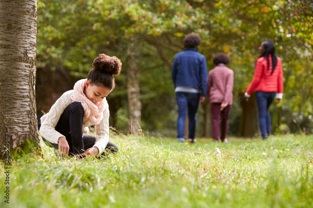 Mixed race girl kneeling in the park to tie her shoe, her family walking in the background, low angle