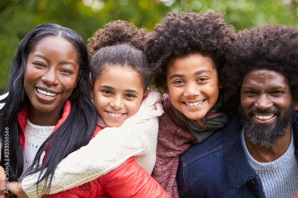 Mixed race family smiling to camera, parents piggybacking kids in the park, close up Mixed race family smiling to camera, parents piggybacking kids in the park, close up