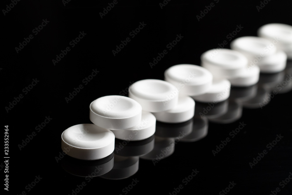Two rows of white pills close-up on a black background with a mirror reflection. Two rows of white pills go away with a perspective. Abstract minimalistic black concept. Same white pills. Two rows of white pills close-up on a black background with a mirror reflection. Two rows of white pills go away with a perspective. Abstract minimalistic black concept. Same white pills.