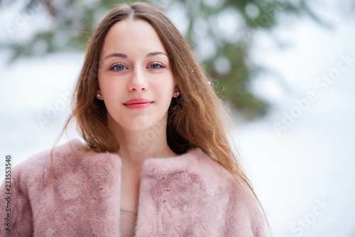 Young beautiful brunette woman in fur coat posing on winter park