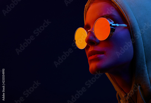 Neon close up portrait of young woman in round sunglasses and hoodie. Studio shot photo