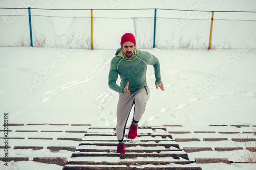 Male athlete with red hat running up the snowy stairs