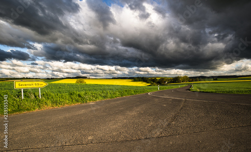 Empty road in the countryside, large dark clouds, sunset light.