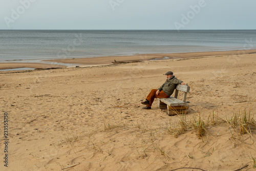 man sitting on a bench on the beach, cloudy, autumn