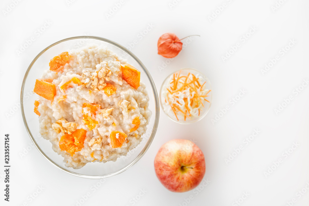 Oatmeal with pumpkin and nuts in a glass plate and fresh apple on a white background. Copy space. Top view Oatmeal with pumpkin and nuts in a glass plate and fresh apple on a white background. Copy space. Top view