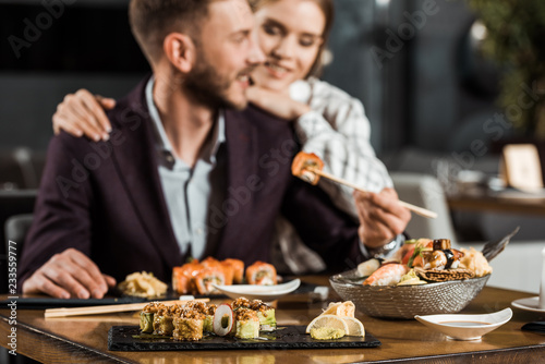 young smiling couple having dinner and eating delicious sushi rolls in restaurant