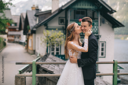 A beautiful wedding couple walks on the lake and mountains background in a fairy Austrian town  Hallstatt.
