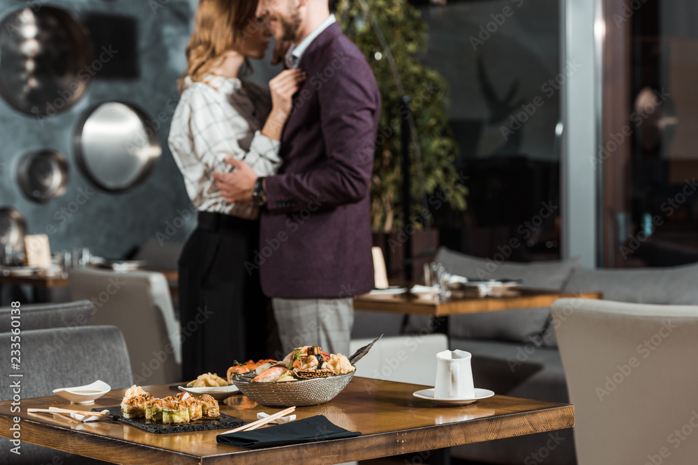 Partial view of beautiful hugging couple dancing behind the table served with sushi in restaurant