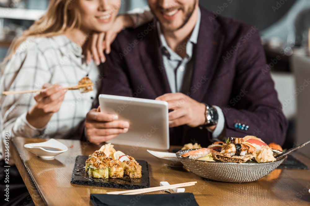 Cropped view of couple using digital device while eating sushi in restaurant