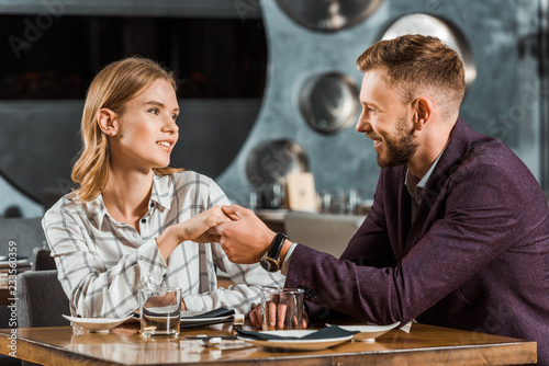 Attractive young adult couple holding hands while sitting in restaurant
