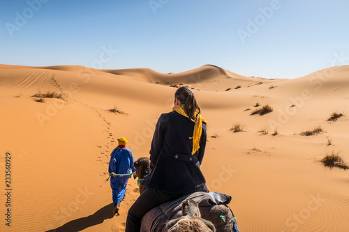 Berber nomad and a young girl riding camel in Sahara desert, Morocco